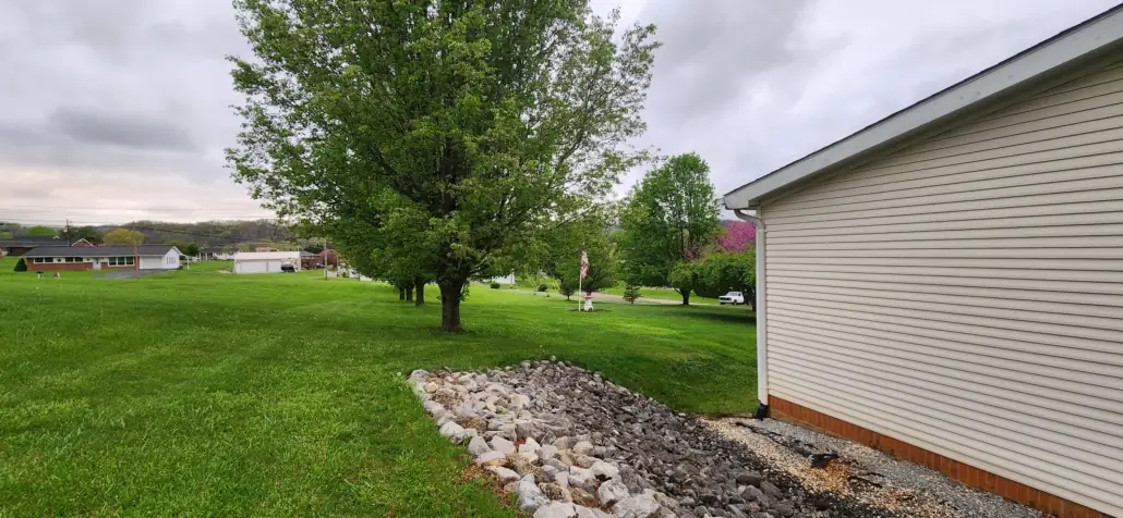 Rock drainage bed and mowed lawn beside a white house