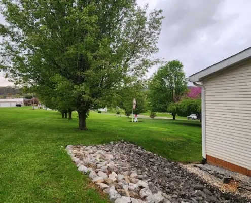 Rock drainage bed and mowed lawn beside a white house